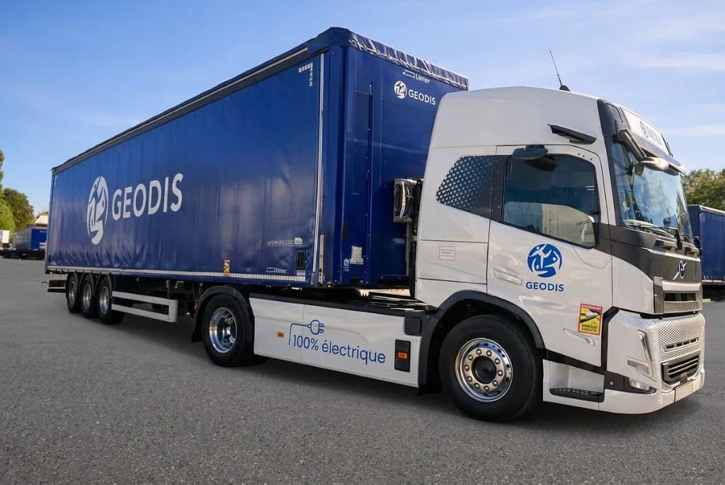 White Volvo electric tractor unit coupled to a blue Geodis curtainside trailer in a depot yard