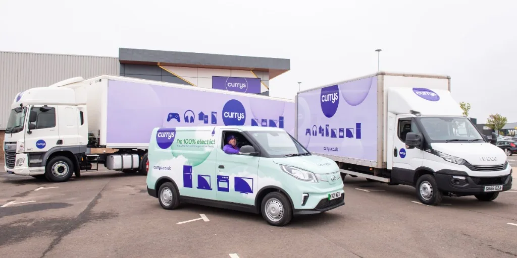 Currys delivery lorries and a small electric van parked in a service-centre yard, the van lettered I’m 100% electric