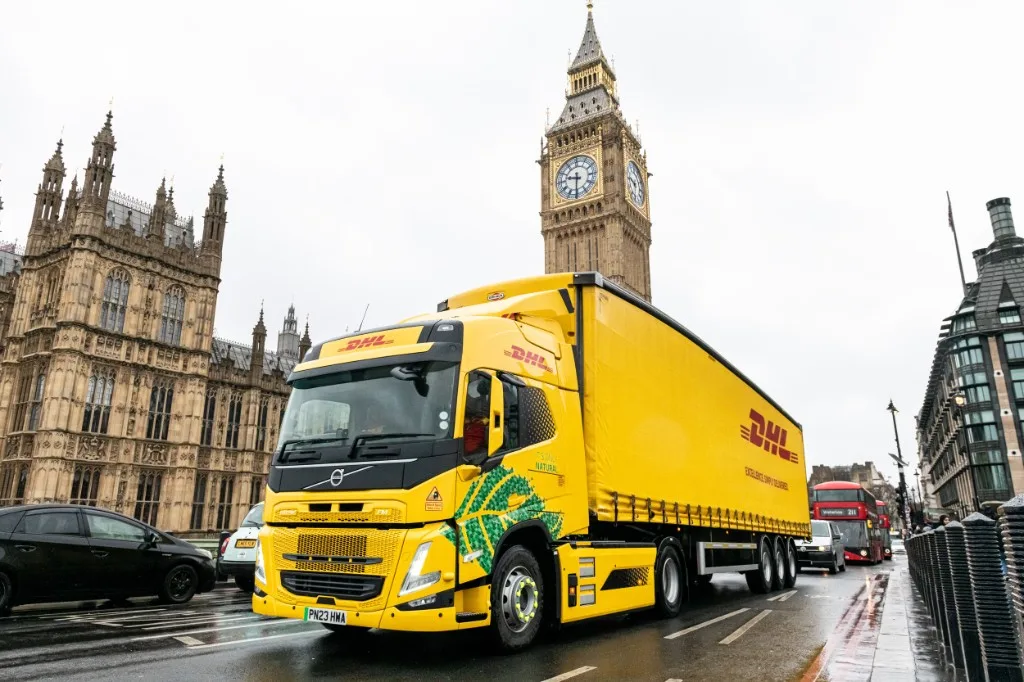 DHL yellow Volvo FM electric heavy goods vehicle passing the Palace of Westminster and Big Ben in London