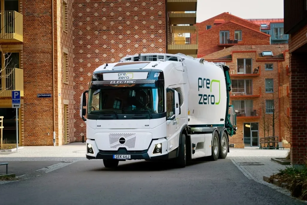 White PreZero electric refuse collection vehicle on a street between brick apartment buildings
